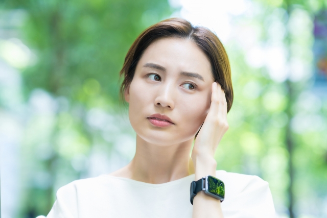 左手を頭に当てて考え事をしている女性