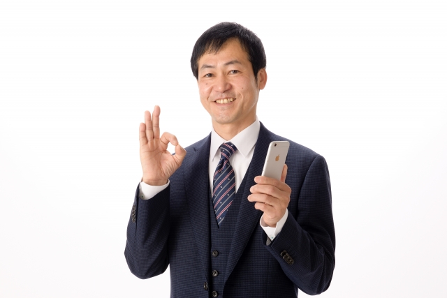 左手にスマホを持ちながらOKサインをしている男性