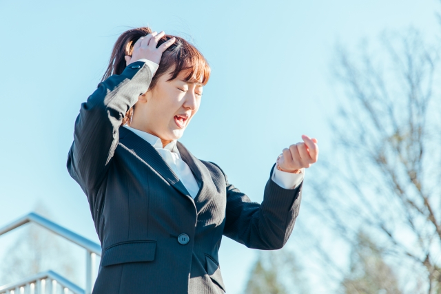 右手を頭に当てながら腕時計を見て困った顔をしている女性