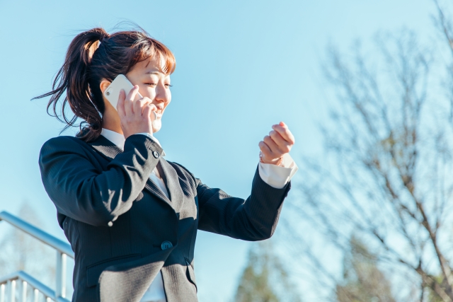 腕時計を見ながらスマホで電話している女性