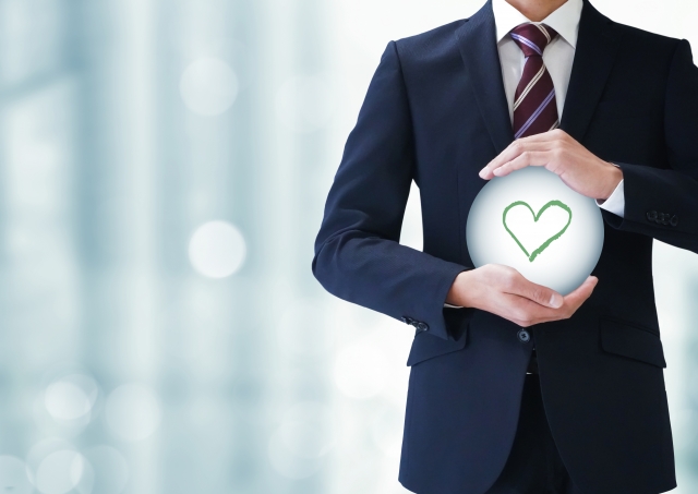 ハートのアイコンが描かれた球体を両手で抱えているスーツ姿の男性