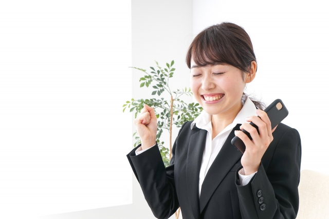 スマホを片手にガッツポーズをしている笑顔の女性