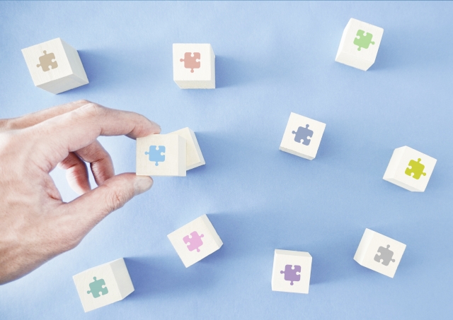 パズルのピースが印字された木製のブロックをひとつ摘み上げている人の手元