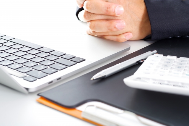 ノートパソコンの前で両手を組んでいる男性の手元