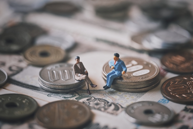 小銭の上に腰掛けている2体のミニチュアの男性