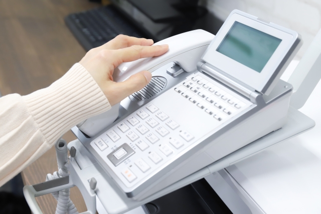 固定電話の受話器に手を添えている女性の手元