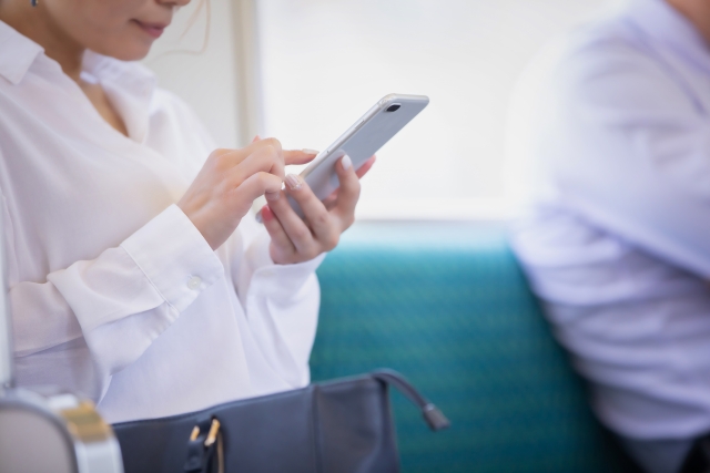 電車のシートに座ってスマホを操作している女性