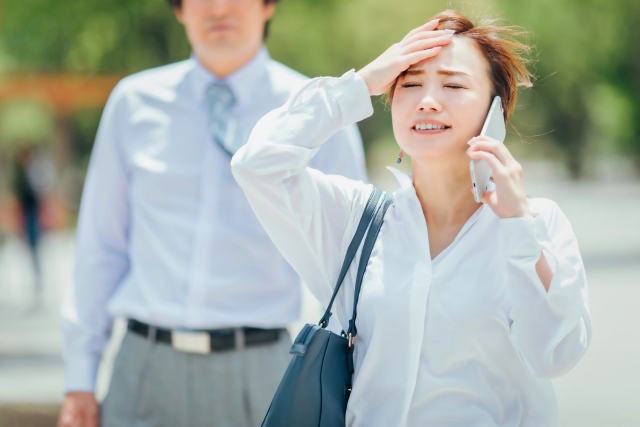 スマホで電話しながら左手を頭に当てている女性