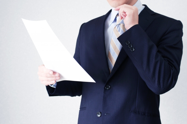 顎の下に手を当てて書類を見ているスーツ姿の男性