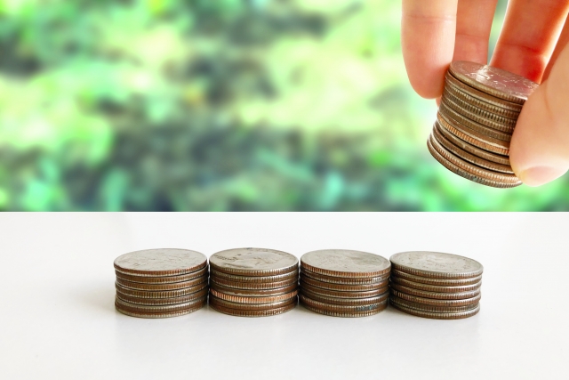 複数枚の硬貨を持ち上げている人の指先と積み上げられた硬貨