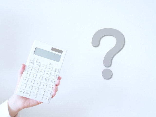 左手に電卓を持っている人の手元とクエスチョンマーク