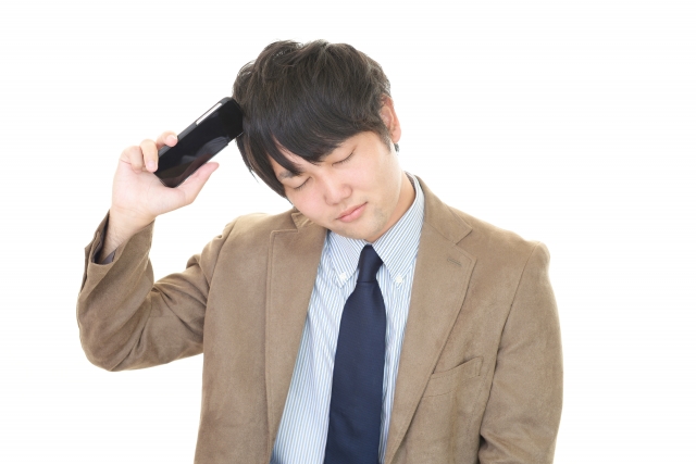 右手に持ったスマホを頭に当てて困った様子の男性