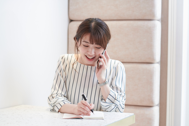 スマホで電話をしながらメモをとっている笑顔の女性