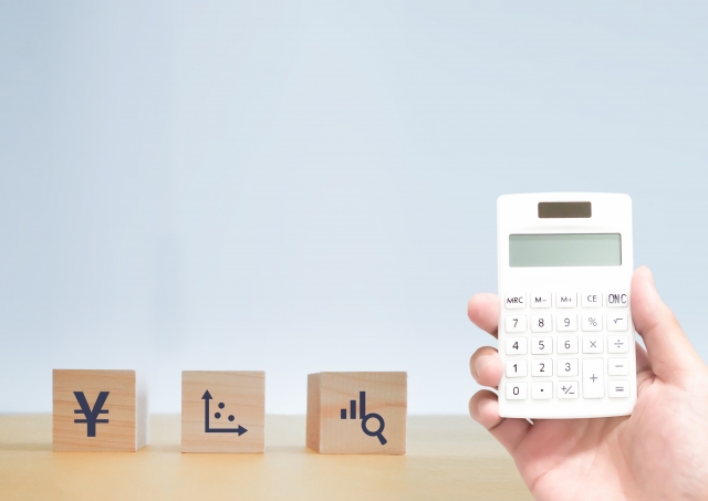 右手に電卓を持っている人の手元と記号が印字された3つのブロック