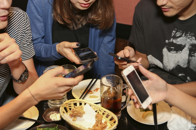 飲み会でスマホを操作している男女4人の手元