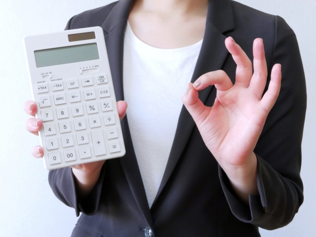 右手に電卓を持って左手でOKサインを出している女性の手元