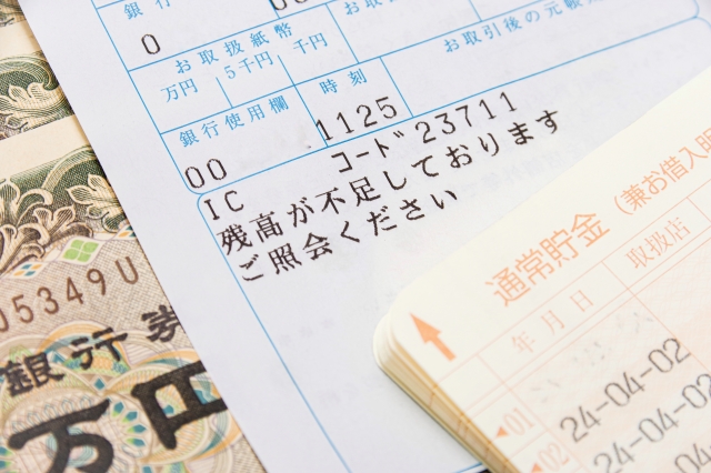 1万円札の上に載っている残高不足の利用明細と貯金通帳