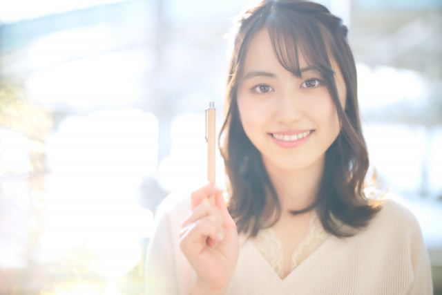 右手にペンを持っている笑顔の女性