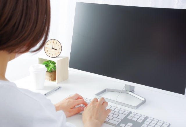 パソコンのキーボードをタイピングしている女性と3時を指すアナログ時計
