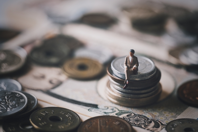 小銭の上に腰掛けているミニチュアの男性