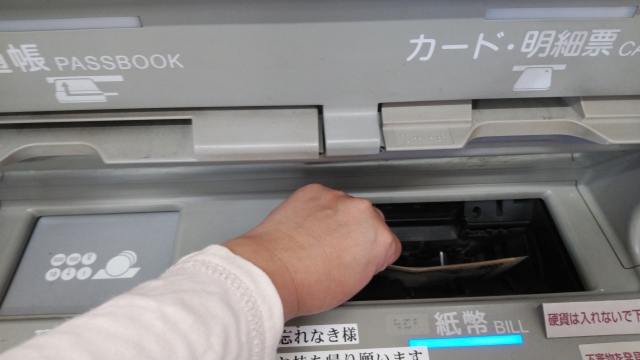 ATMの投入口にお札を入れている人の手元