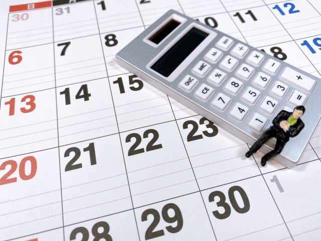 カレンダーの上に置かれた電卓に腰掛けている男性のミニチュア