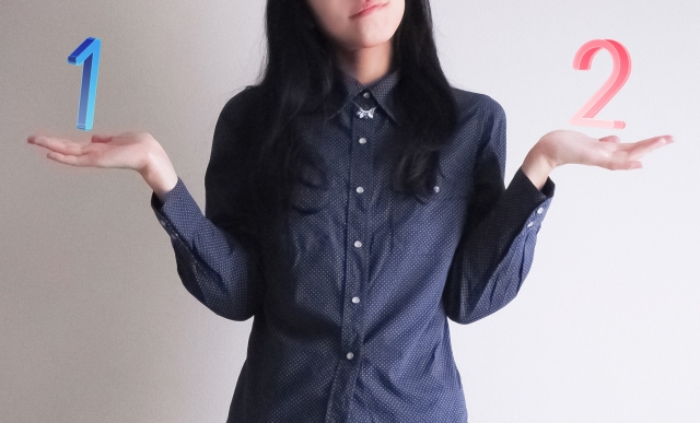右手に1の数字左手に2の数字を浮かべて悩んでいる女性