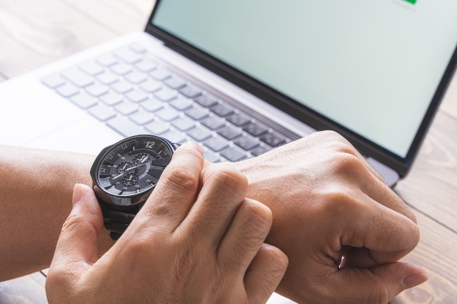 パソコンの前で腕時計を見ている男性の手元