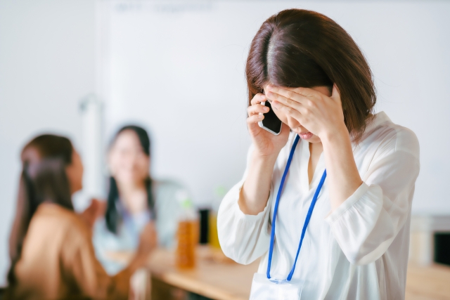 スマホで電話しながら左手を頭に添えて下を向いている女性