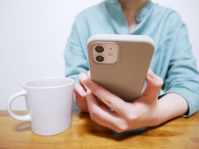 座ってスマホを操作する女性の手元とマグカップ