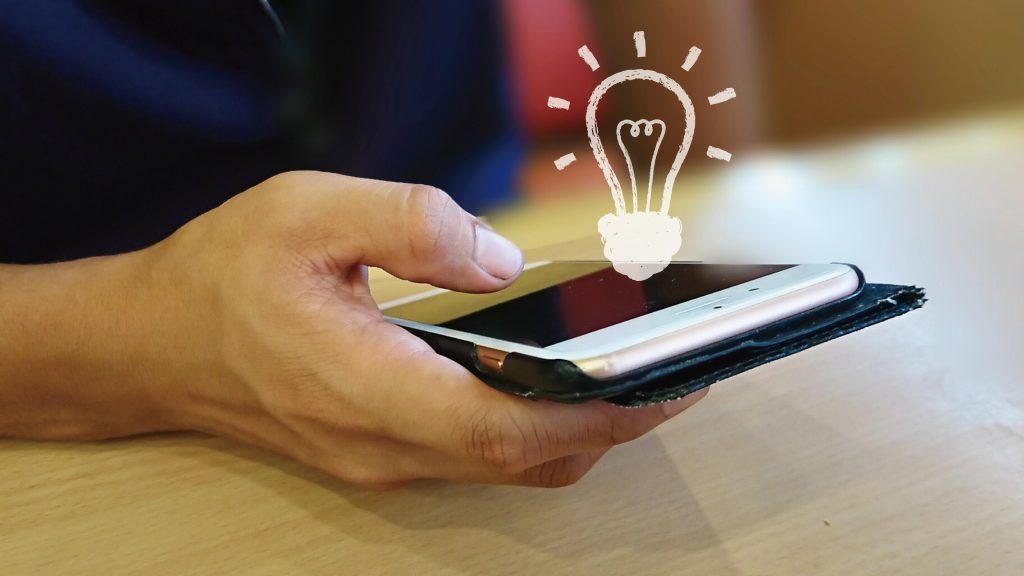 右手でスマホを操作している人の手元と電球のアイコン