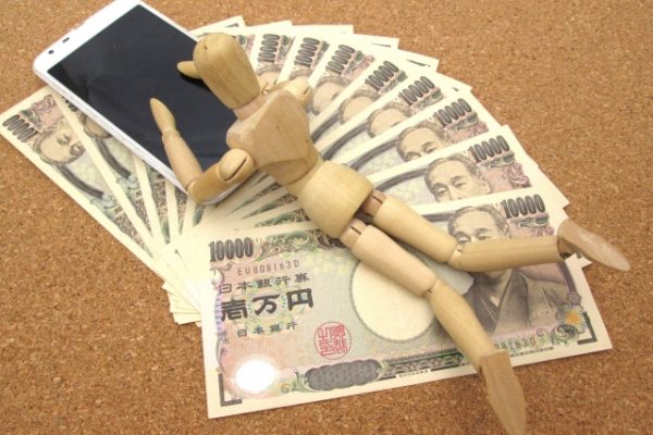 扇状に並べられた1万円札の上に置かれたスマホとデッサン人形