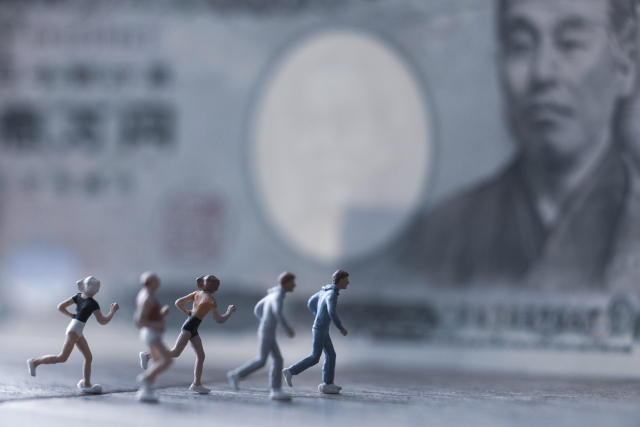 一万円札の隣で走っているミニチュアの人々