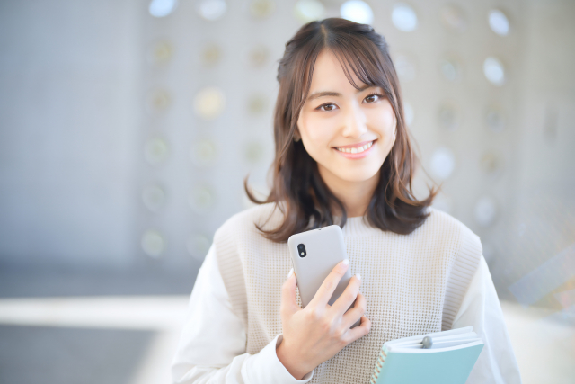 ノートとスマホを持って微笑む女性
