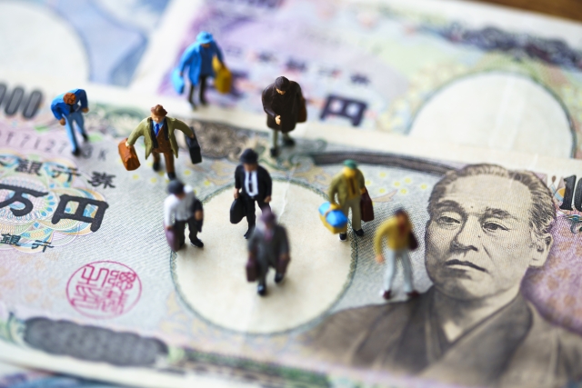 1万円札の上に並べられた複数のミニチュアのビジネスマン