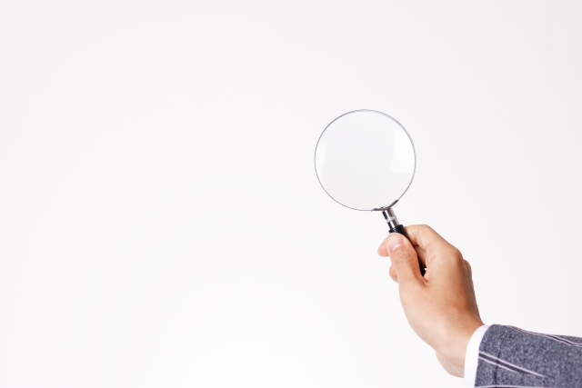 右手で虫眼鏡を持つ男性の手元