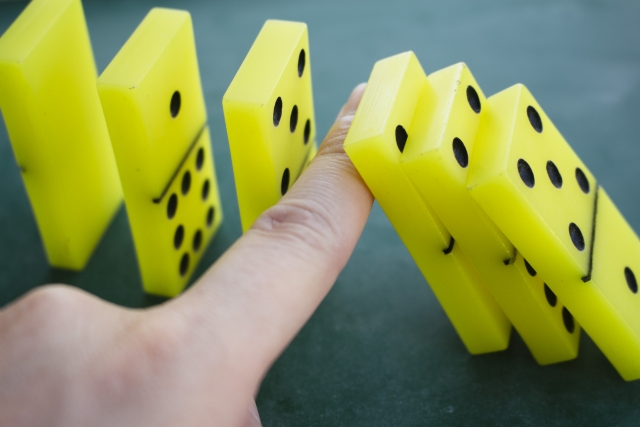 並んだドミノが倒れるのを防いでいる人の指