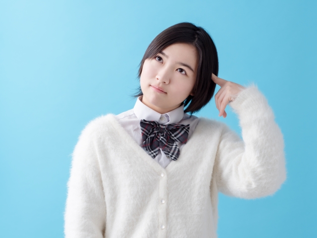 人差し指を頭に当てて考えている様子の女子高生