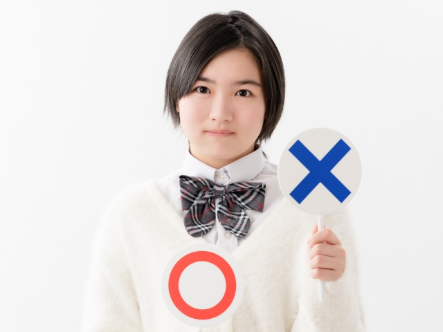 ×マークのサインを出している女子高生