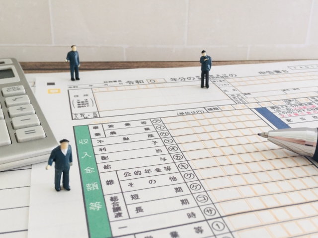 確定申告書の上に並んだ3体のミニチュアの男性