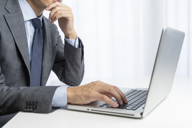 ノートパソコンの前で考えている様子の男性