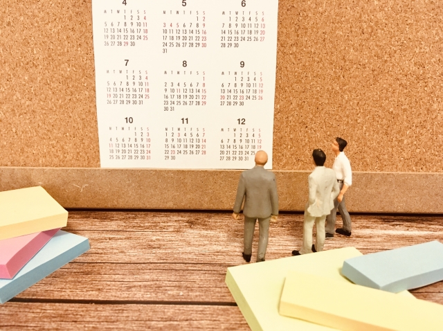 年間カレンダーの方を向いている3人の男性のミニチュア