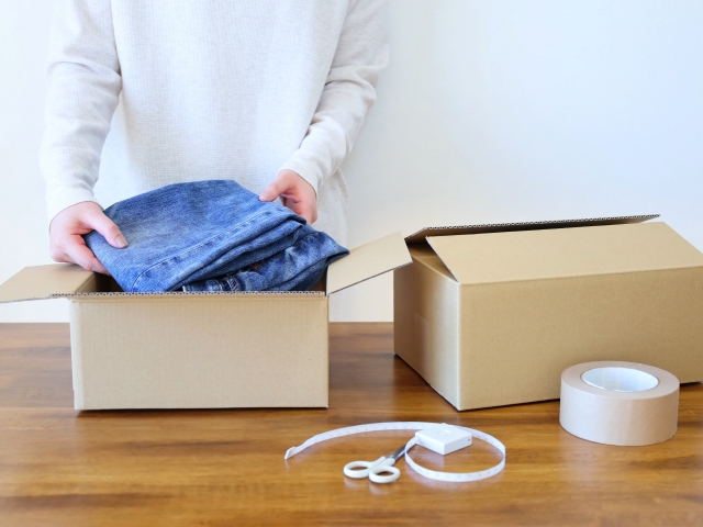 段ボールに服をつめる女性の手元
