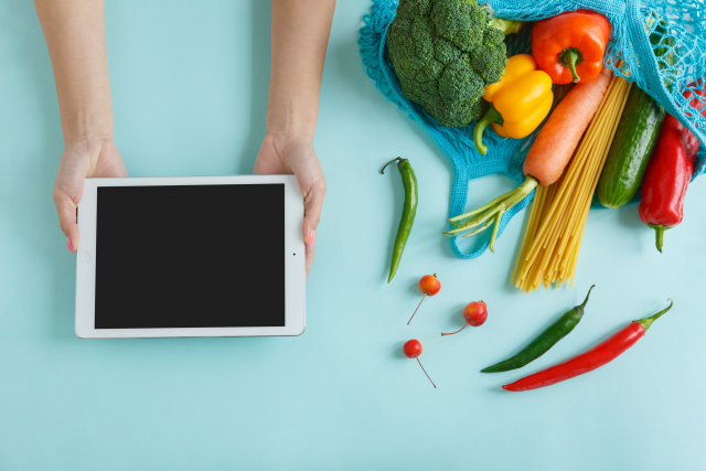 タブレットを両手で持っている女性の手元と野菜
