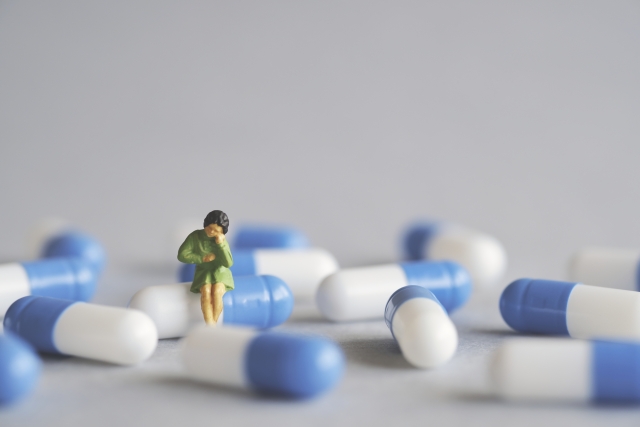 カプセル剤に腰掛ける女性のミニチュア