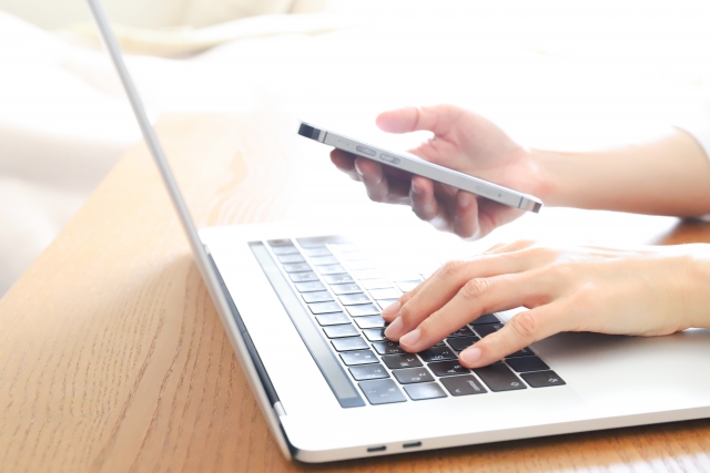 ノートパソコンの前でスマホを操作している女性の手元