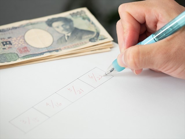 数枚のお札と紙に日付を書いている人の手元