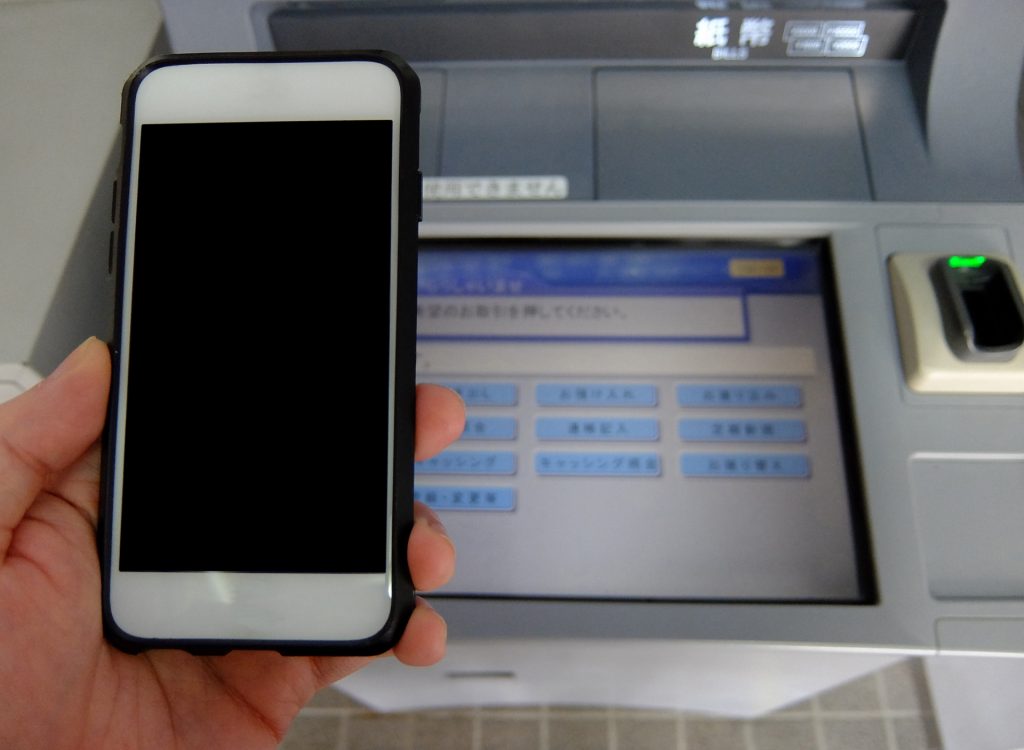 自動契約機の前で左手でスマホを操作している人の手元