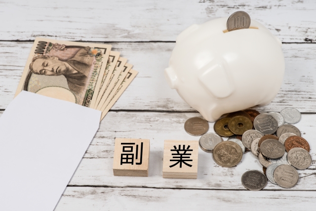 副業と印字された木製のブロックとその両脇に並べられたお札と小銭