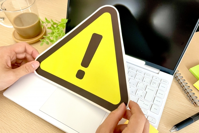 ノートパソコンの前で注意看板を持つ手元